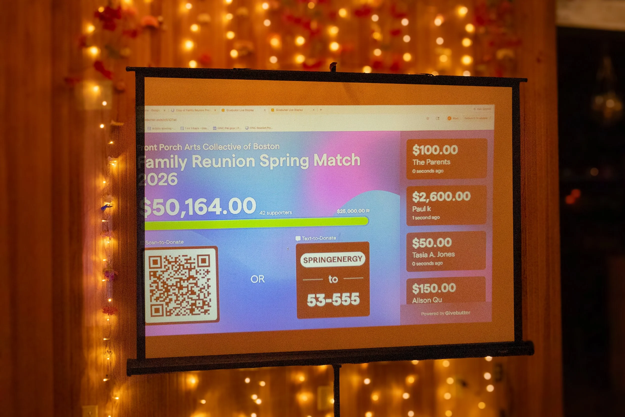 An electronic fundraising display screen shows the details for a charity event called 'Family Reunion Spring Match 2026' with a total of $50,164.00 raised from 42 supporters. The screen also shows recent donations of $100, $2,600, $50, and $150 from 