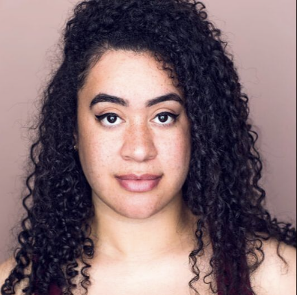 A woman with curly black hair and light skin, looking at the camera with a neutral expression.