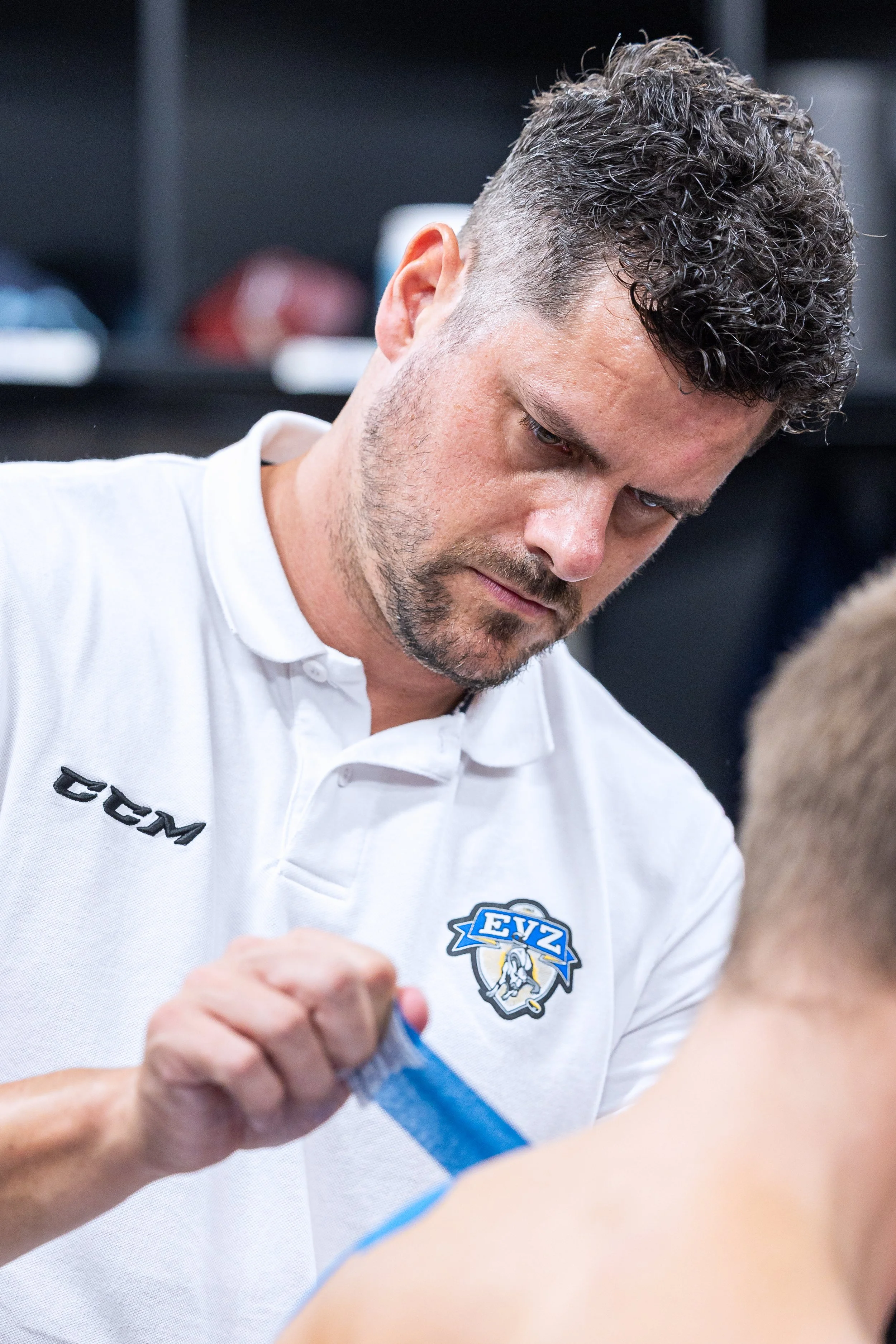 Hockey coach wrapping a player’s hand with athletic tape in a locker room.