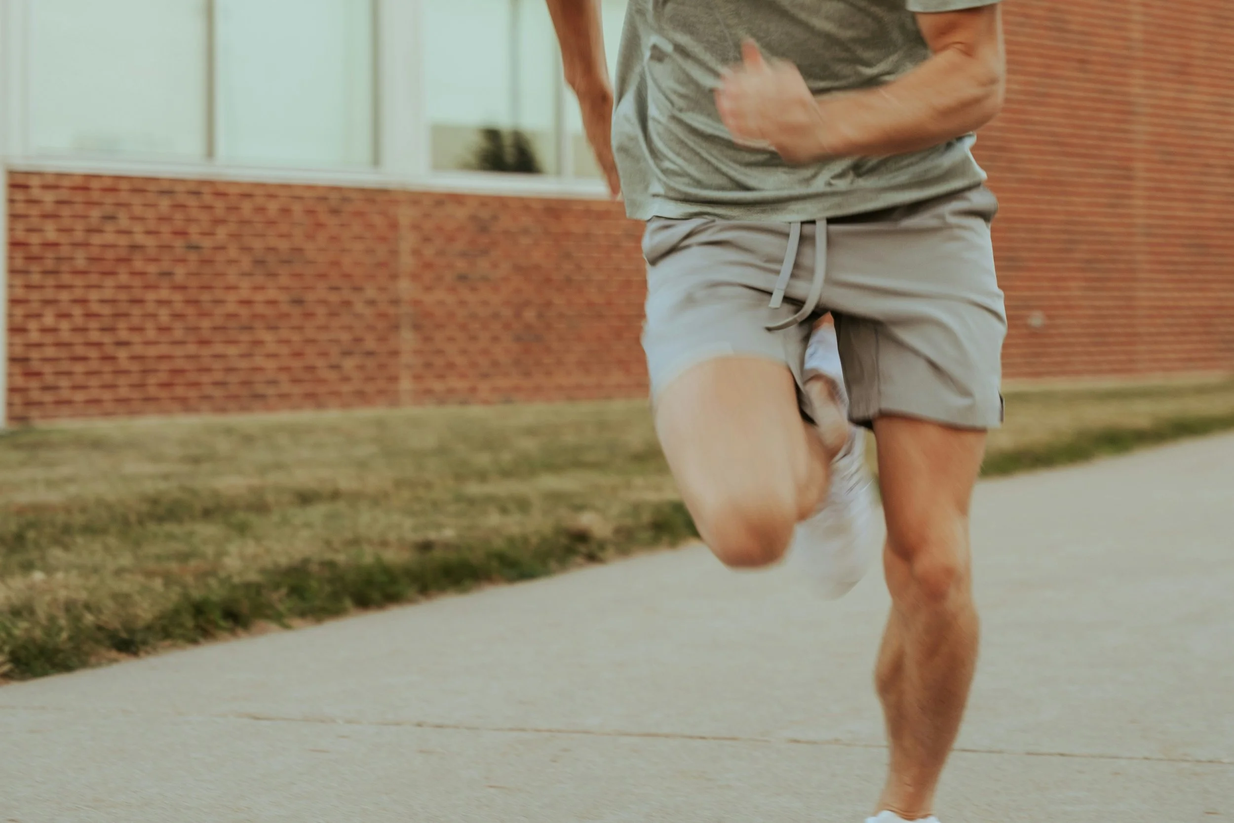 A person running outdoors on a sidewalk near a brick building, only the lower half of their body is visible.