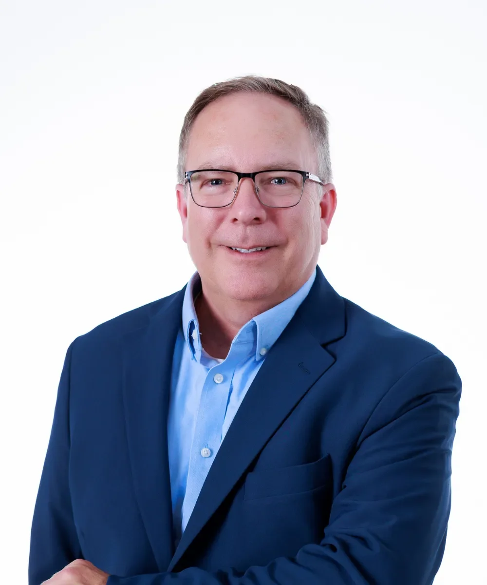 A middle-aged man in a blue suit and glasses smiling for a professional headshot against a white background.