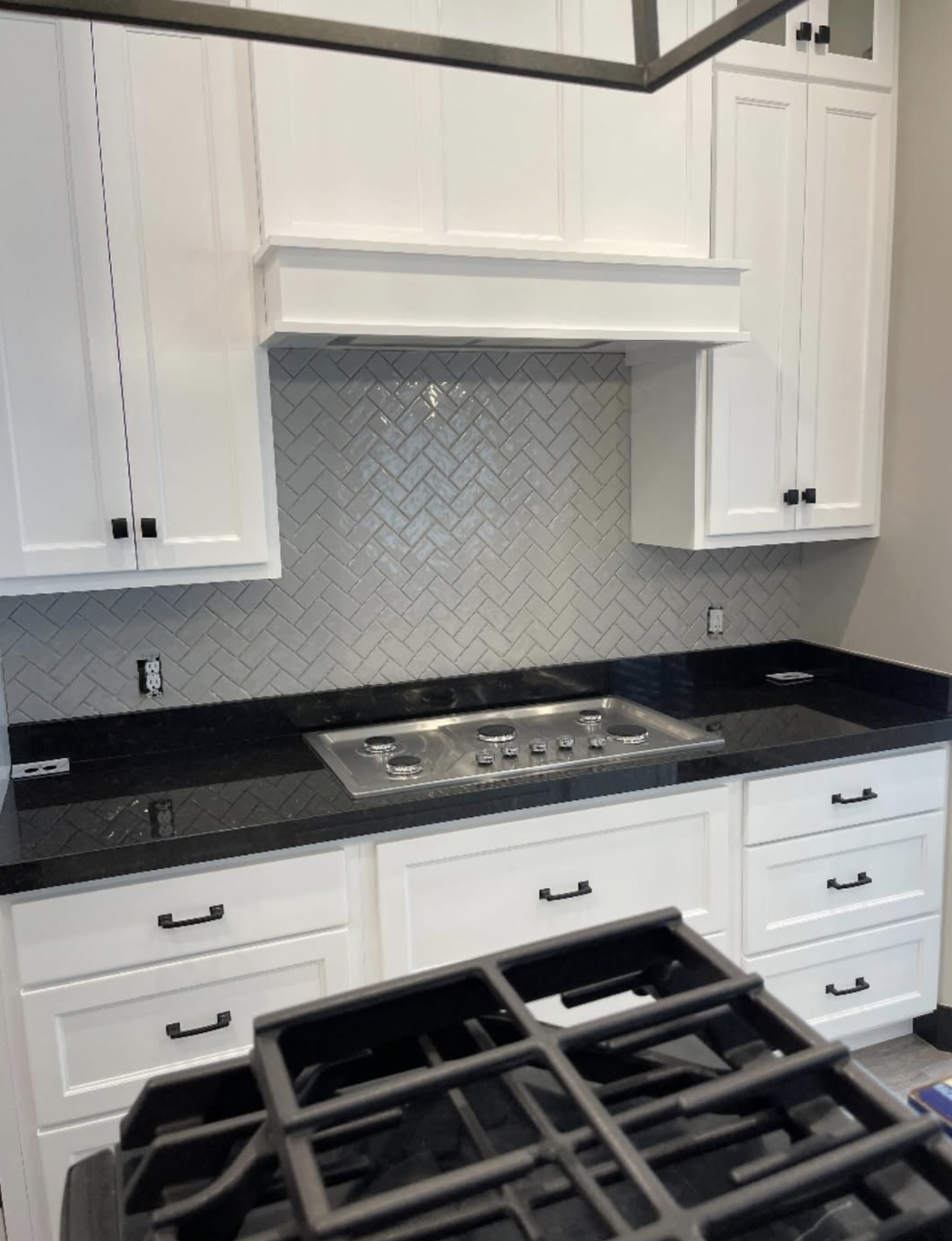 Kitchen with white cabinets, black countertop, herringbone tile backsplash, and a stovetop.