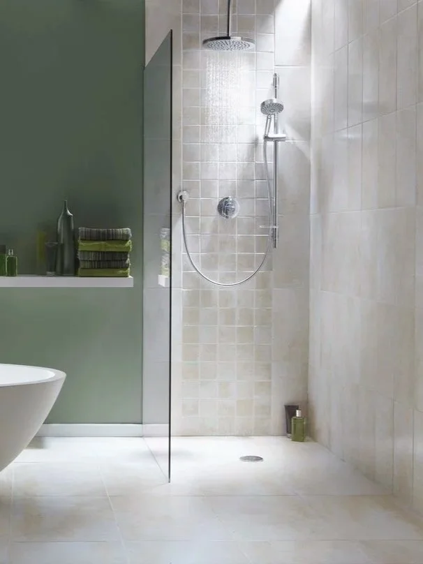 Minimalist bathroom with a green wall, a bathtub, and a walk-in shower with beige tiles and a sliding glass door.