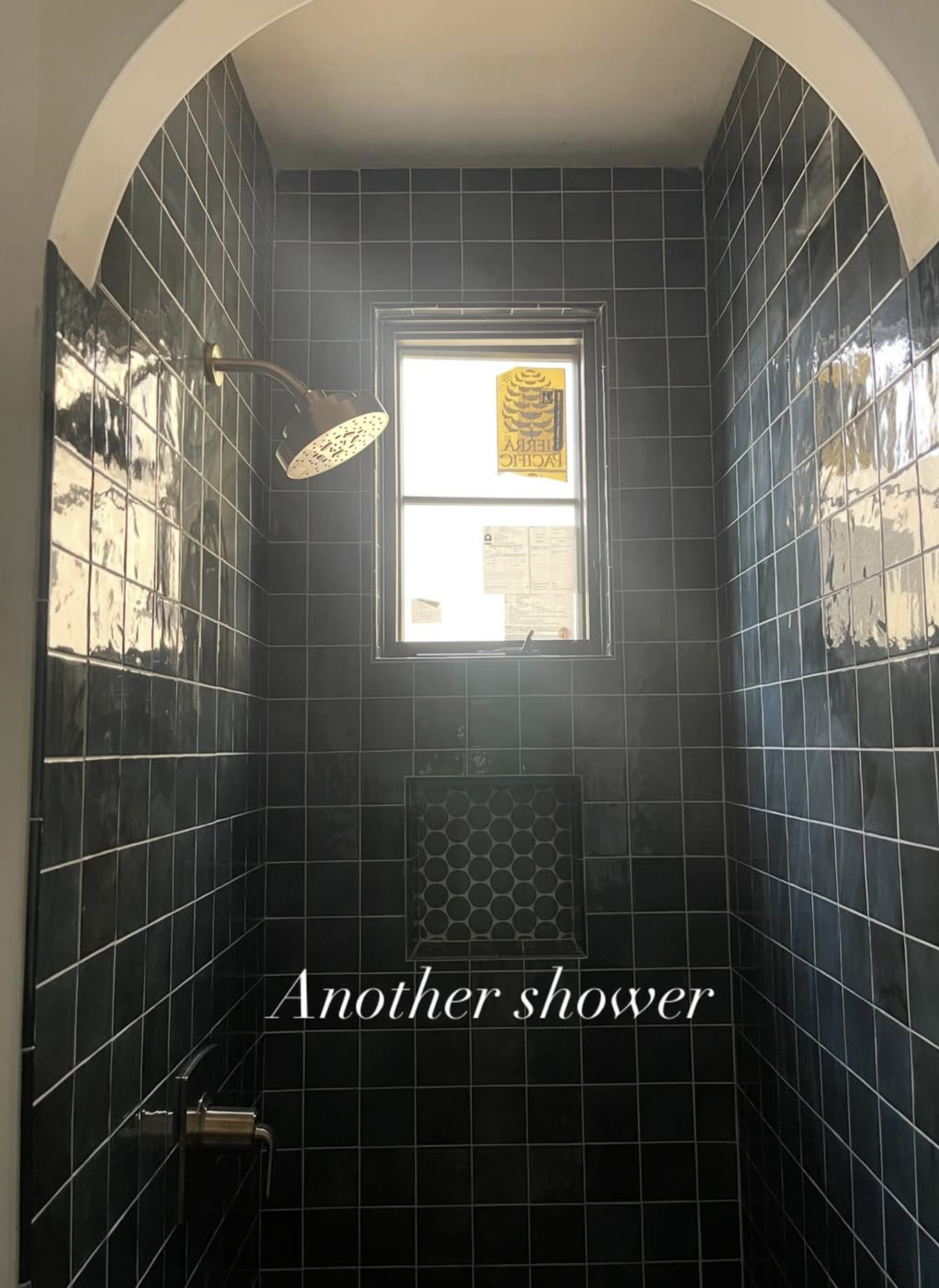 Inside a small shower with black tiled walls, a window at the far end, and a silver showerhead on the left side. The text 'Another shower' is overlaid on the image.