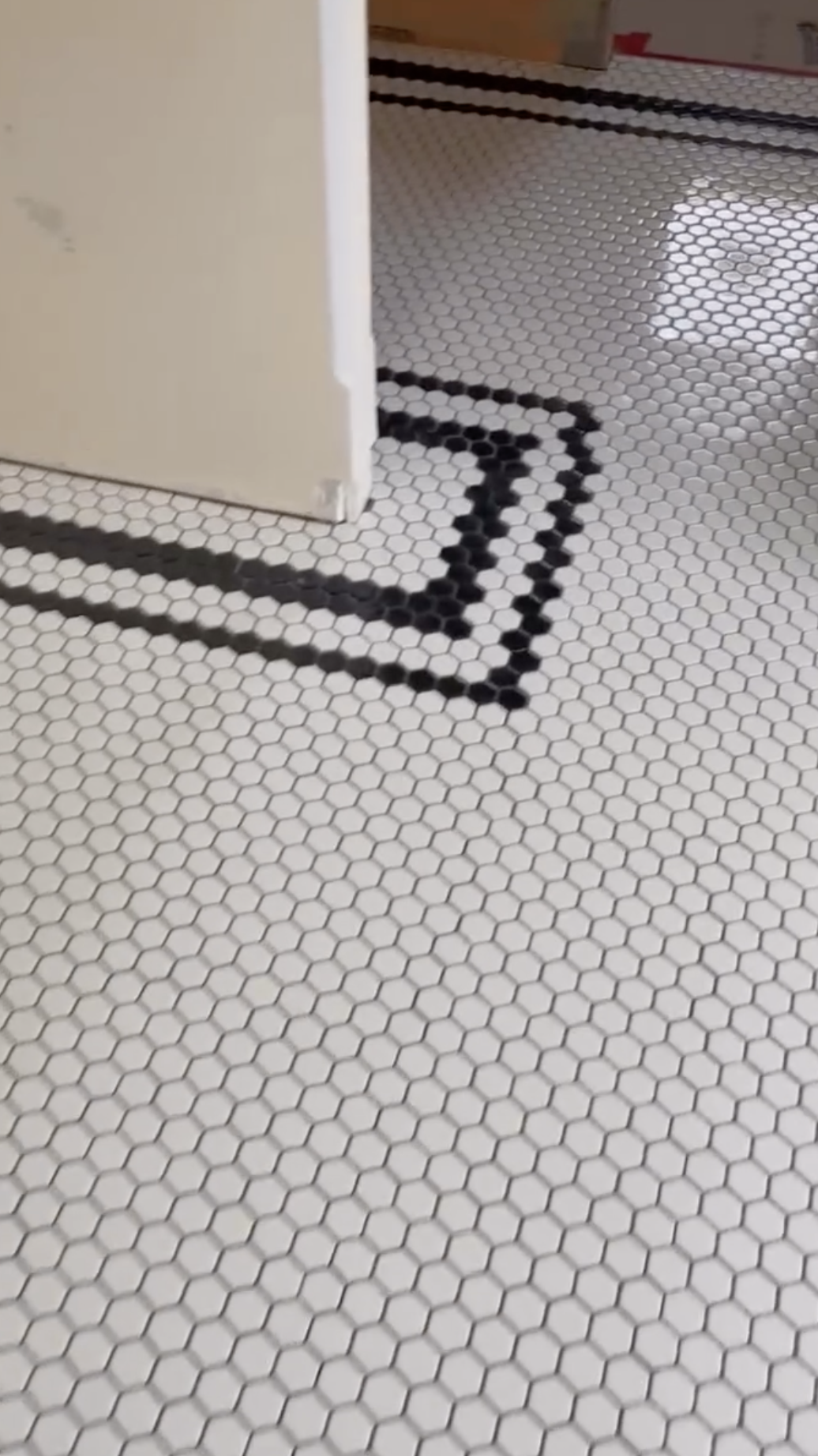 White tiled floor with black hexagonal tiles forming a curved arrow pattern leading into a doorway.