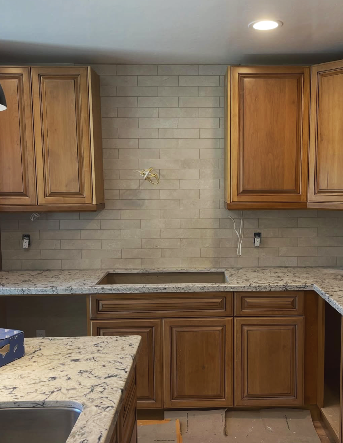 Kitchen with wooden cabinets, granite countertops, beige tile backsplash, and no appliances installed yet.