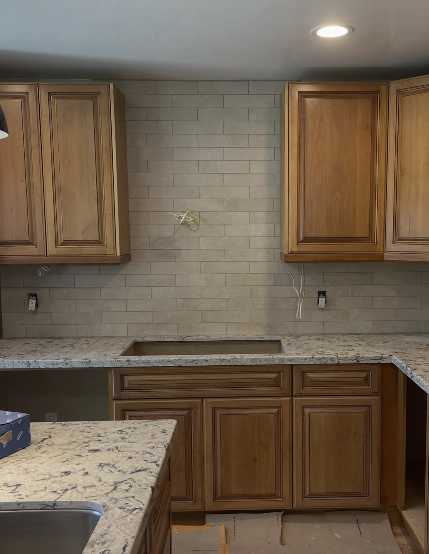 Photo of a kitchen under renovation with unfinished countertops, wooden cabinets, and electrical wiring visible.