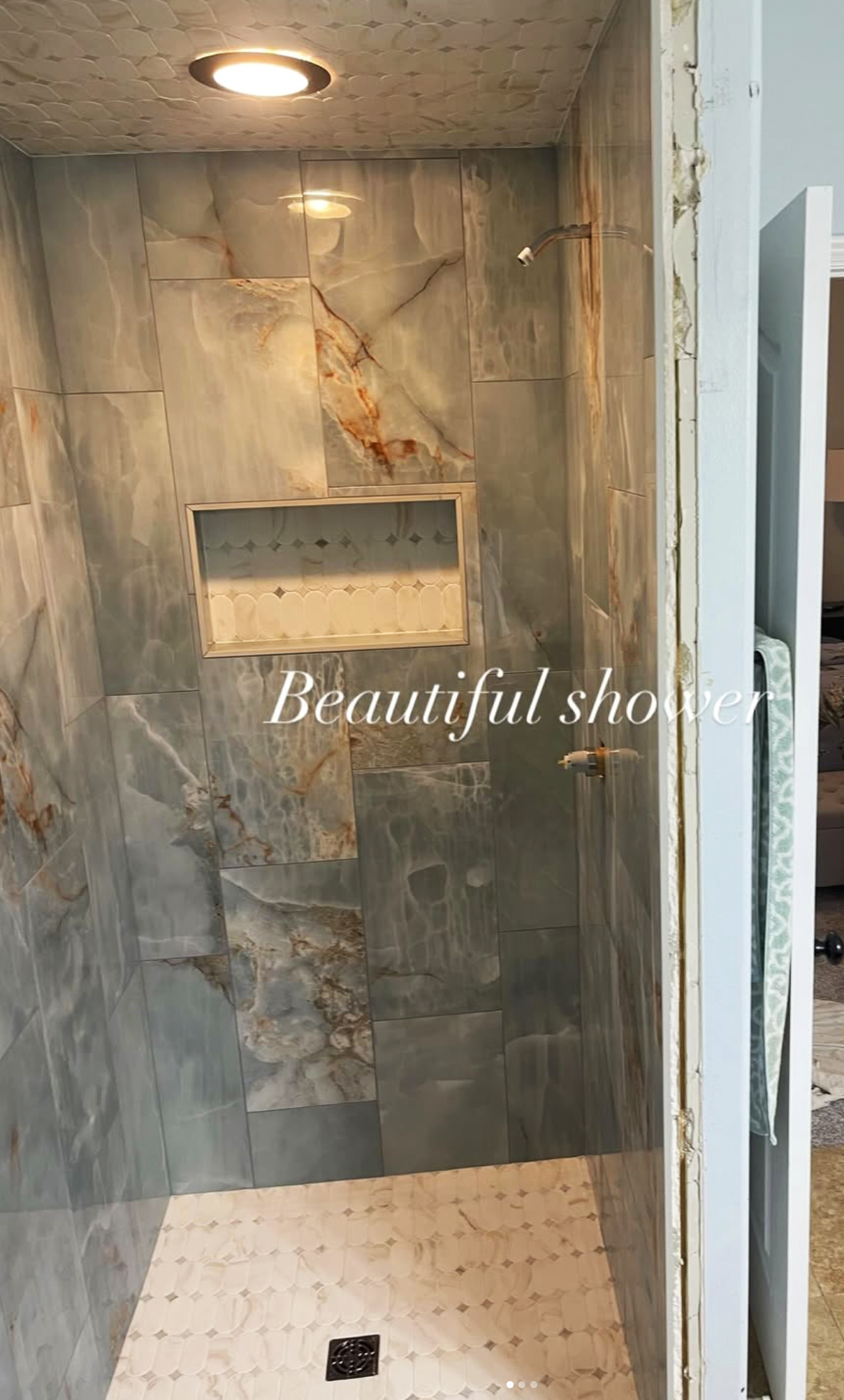 A partially finished walk-in shower with gray and brown marble tiles, a built-in shelf, a ceiling light, and an incomplete door frame.