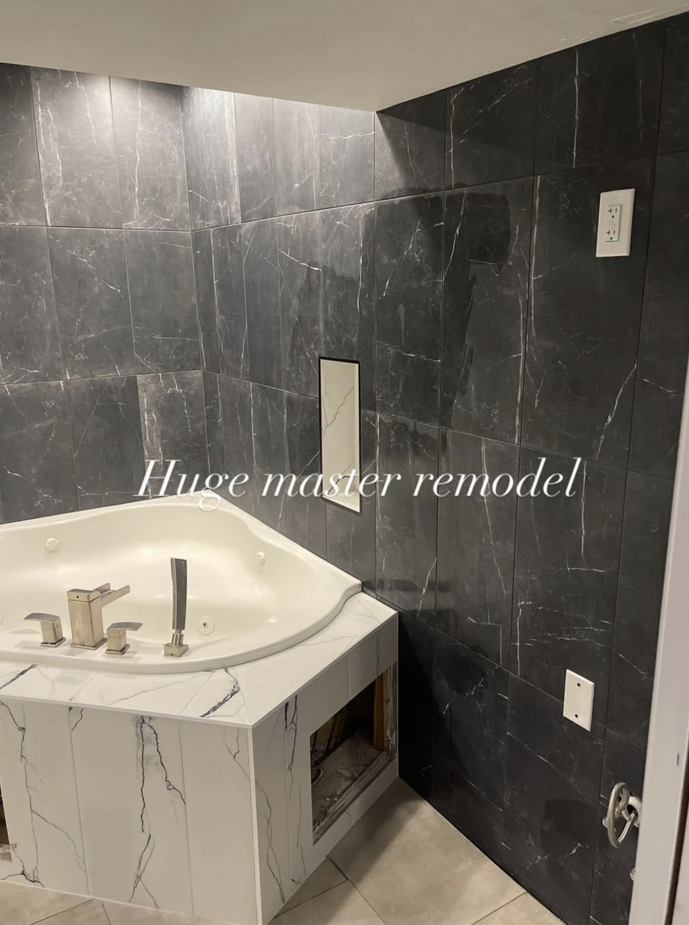 Bathroom with marble tiles, a white bathtub with modern fixtures, and a wall repair opening. Text overlay reads 'Huge master remodel.'