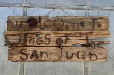 A rustic wooden sign with handwritten text that reads 'Welcome to the San Juan,' attached to a tiled wall.