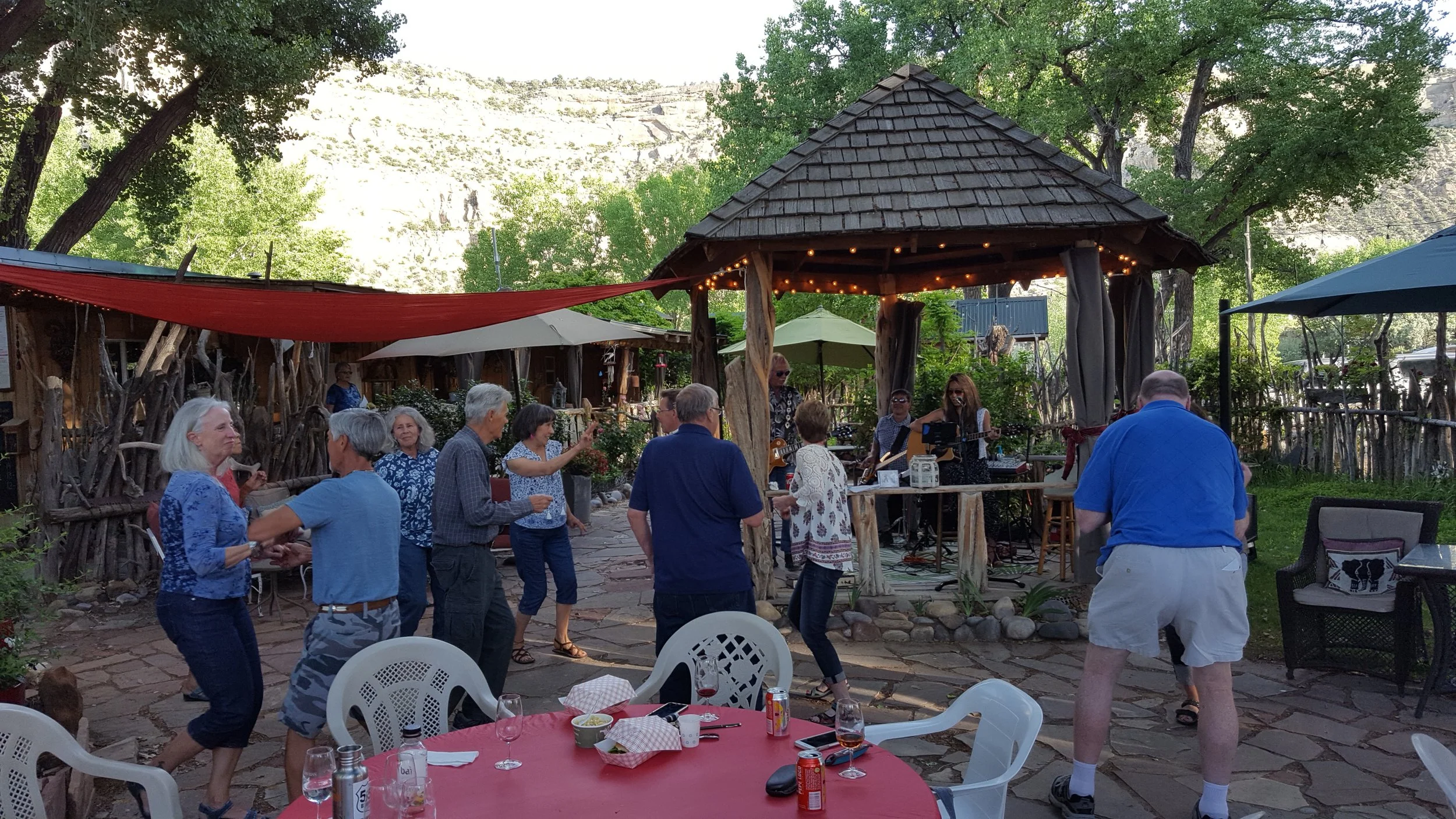 People dancing and listening to live music at Wines of the San Juan in an outdoor rustic setting with trees, stone patio, and tables with drinks
