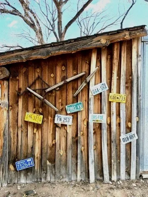 A wooden shed with a collection of old, rusty farming tools and license plates hanging on the exterior wall.