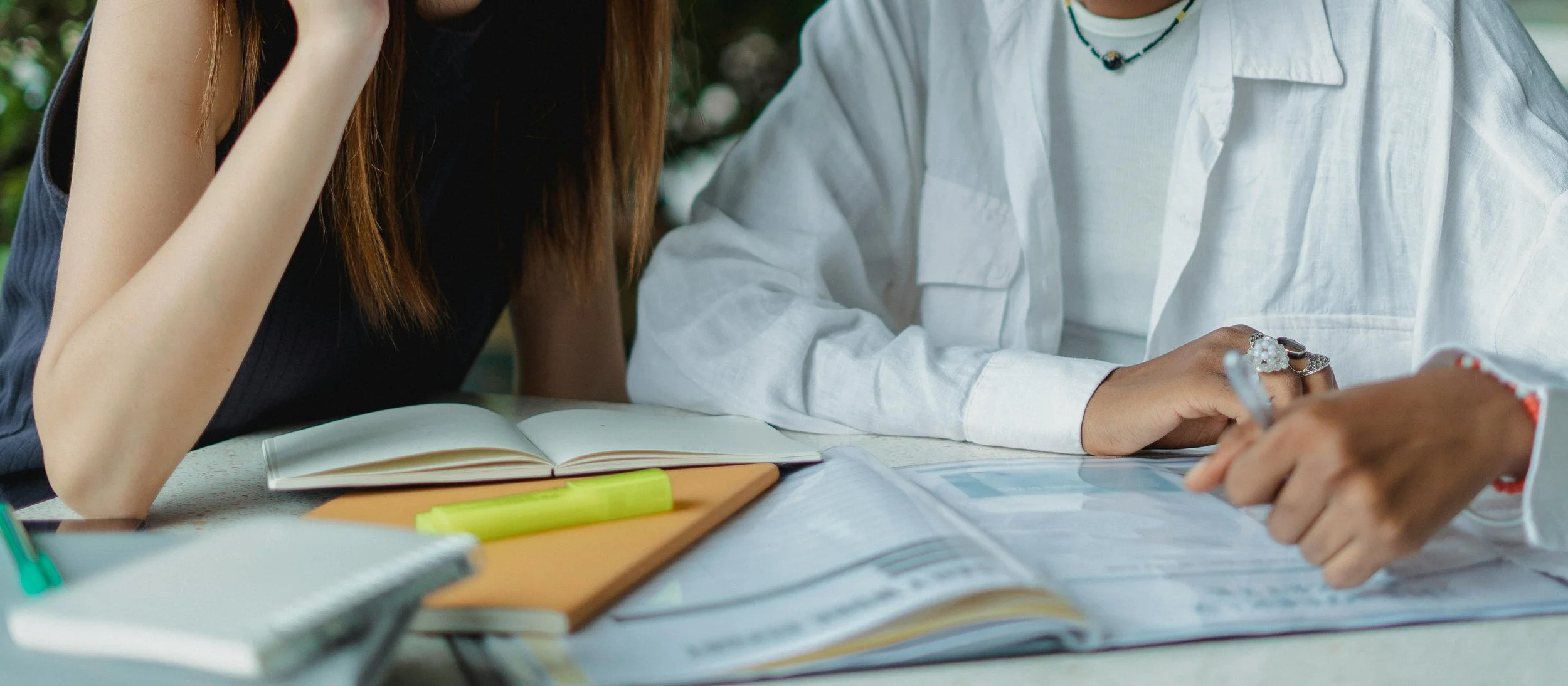 Two people studying together at a table with notebooks, highlighters, and a tablet.