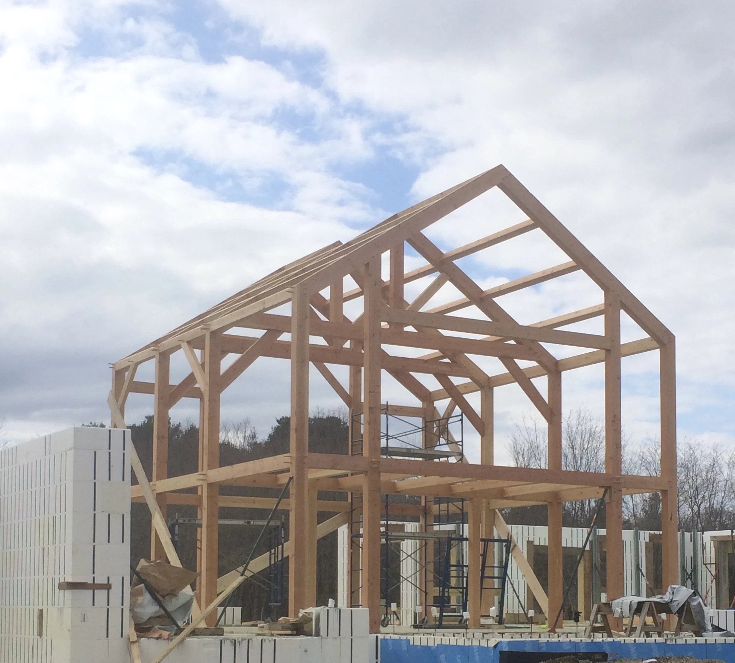 Wooden frame of a house under construction with scaffolding and construction materials around.