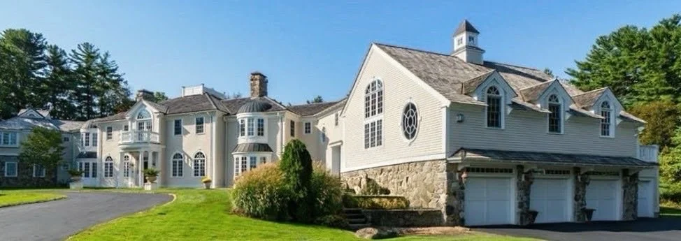 Large, elegant white house with multiple roofs, stone foundation, and large windows