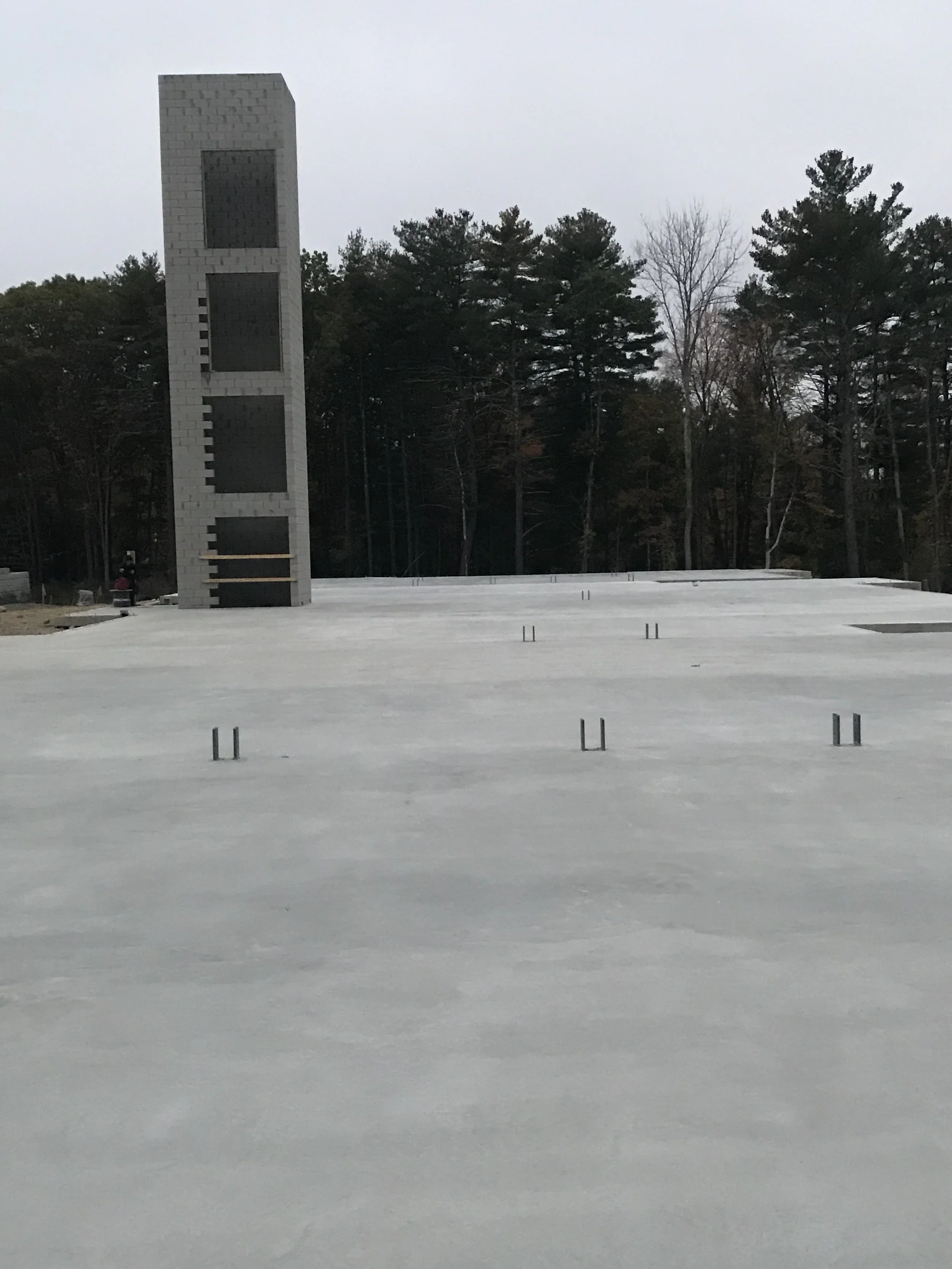 Construction site with a concrete slab foundation, metal pipe protrusions, and a tall unfinished tower