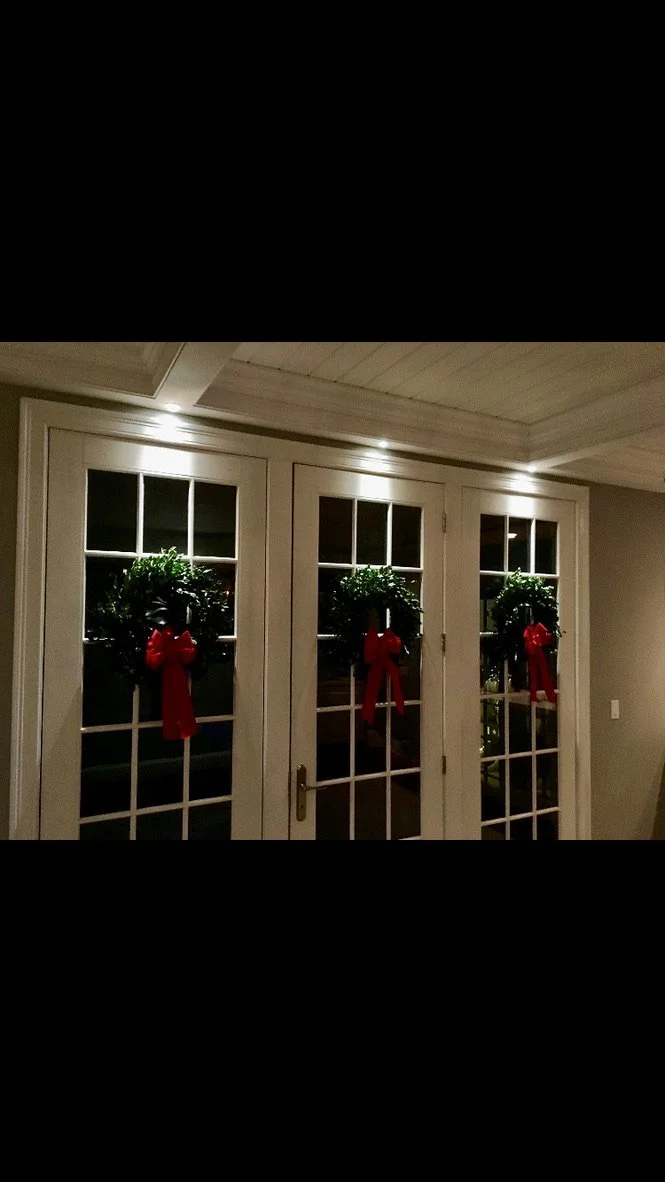 Three glass-paneled doors decorated with Christmas wreaths and red bows in a warmly lit room.