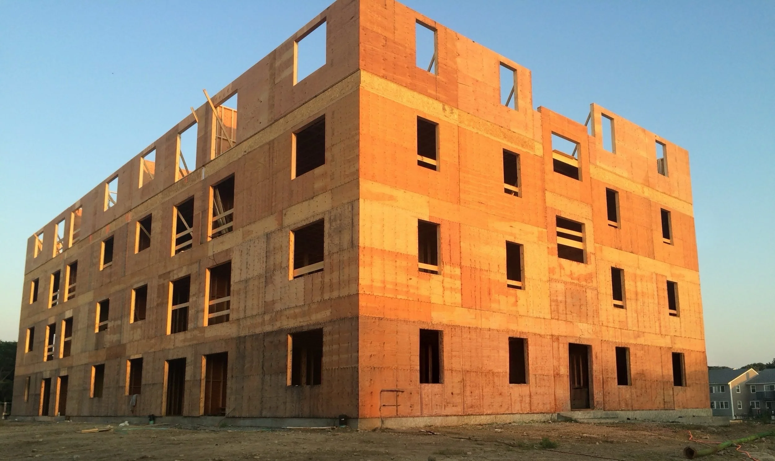 A multi-story building under construction with exposed wooden framing and open window spaces