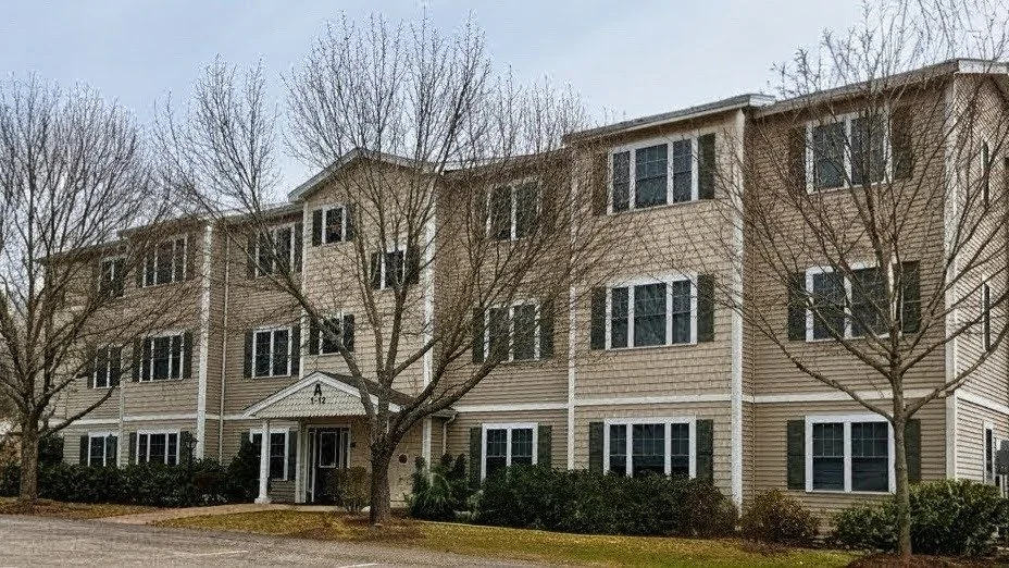 Three-story residential apartment building with beige siding, multiple windows