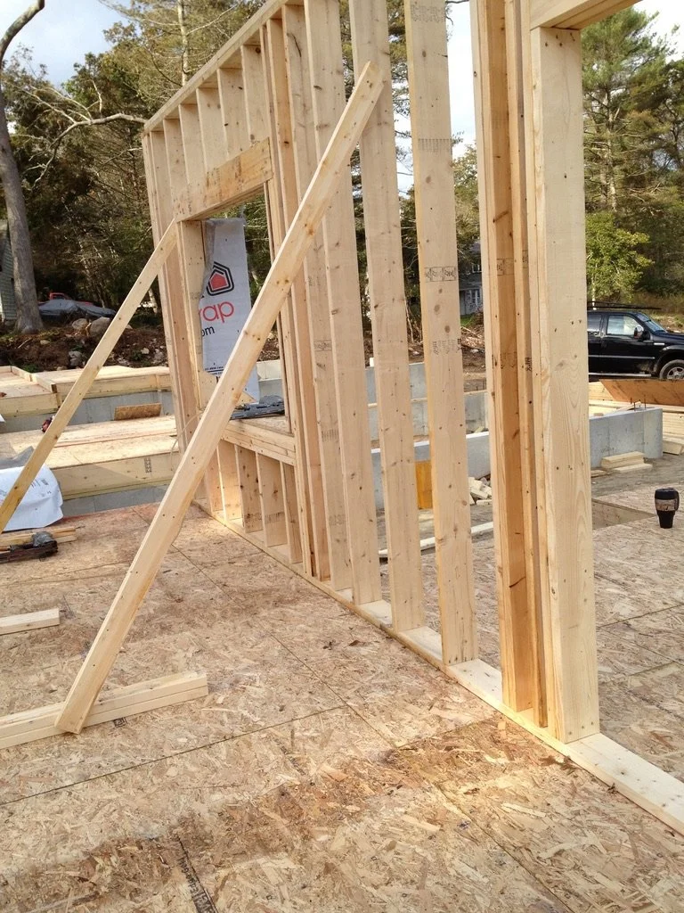 Wooden framing for a house under construction with vertical and horizontal studs, supported by diagonal braces.