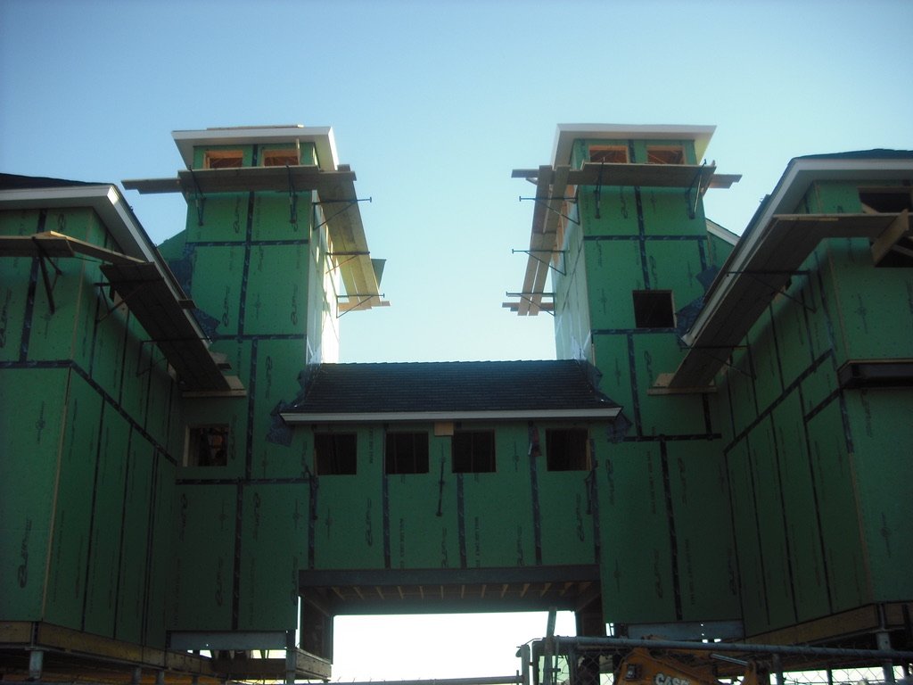 Construction site with a building under construction featuring green exterior sheathing, two prominent vertical towers with small structures at the top