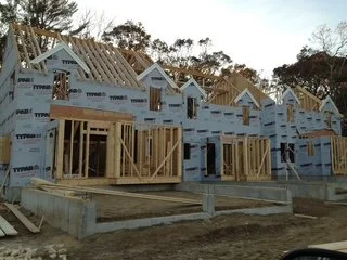 Rows of houses under construction, with wooden frames and blue protective sheathing, on a construction site 