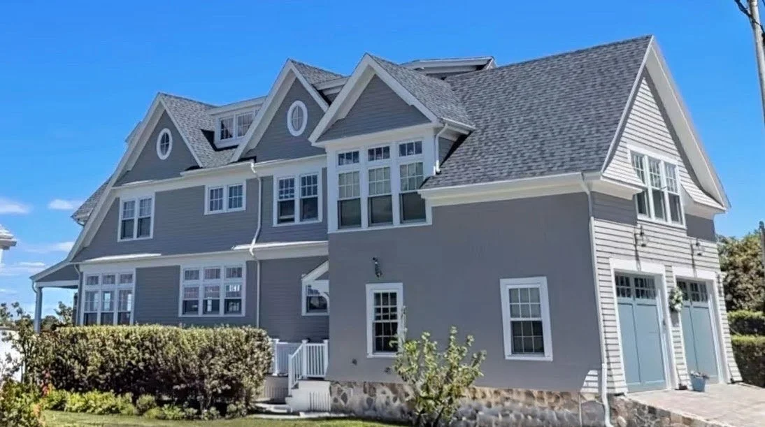 A large gray house with multiple gabled roofs, white trim, and large windows