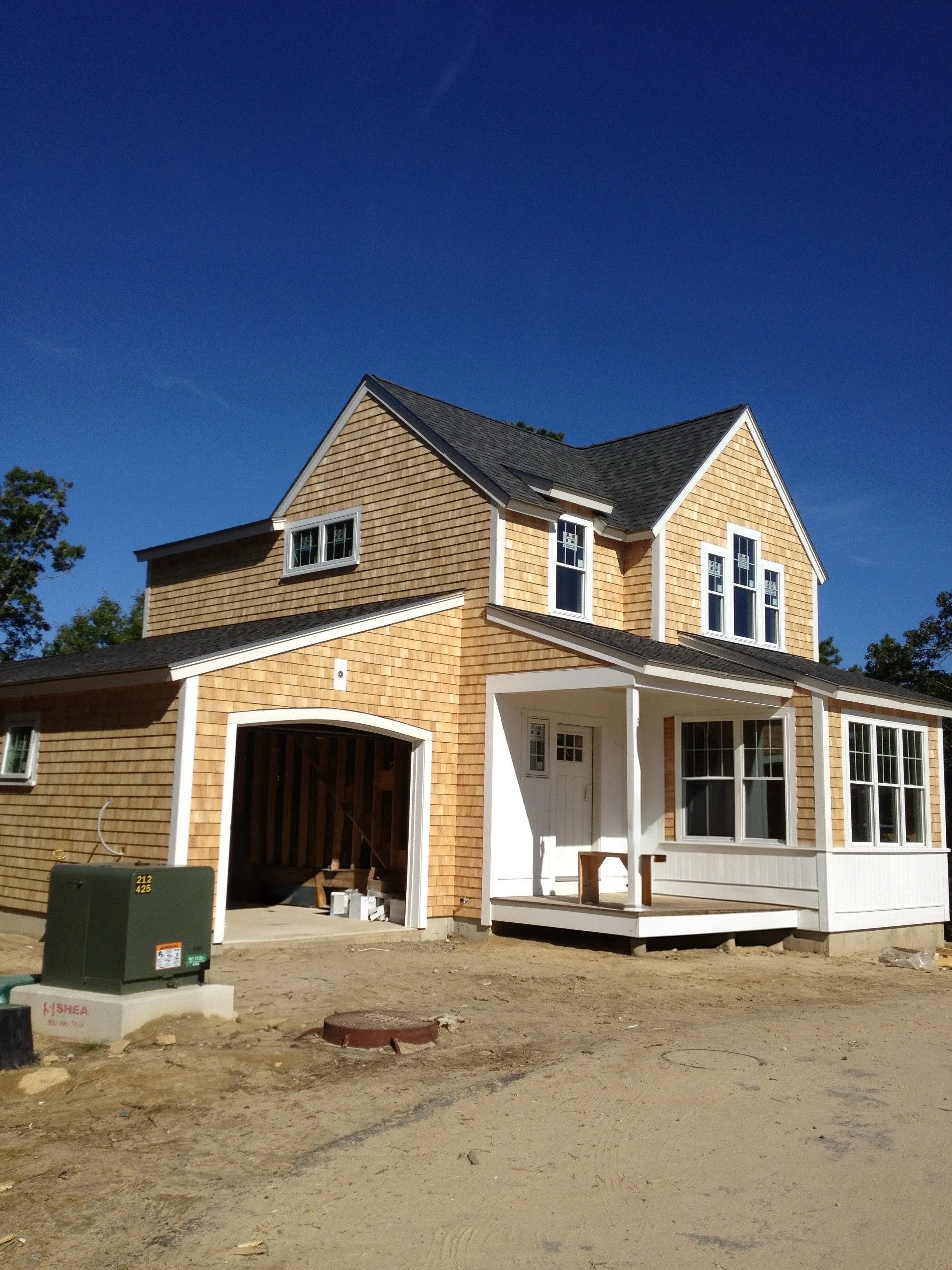 A two-story house under construction with light brown siding, multiple windows, and a small front porch