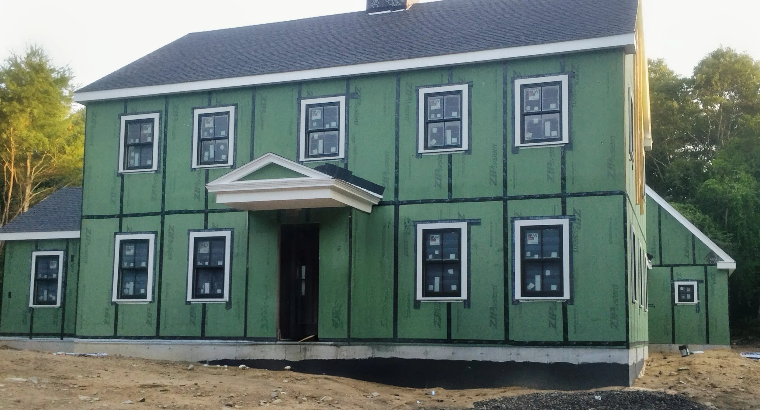 A two-story house under construction with green sheathing and black window frames.