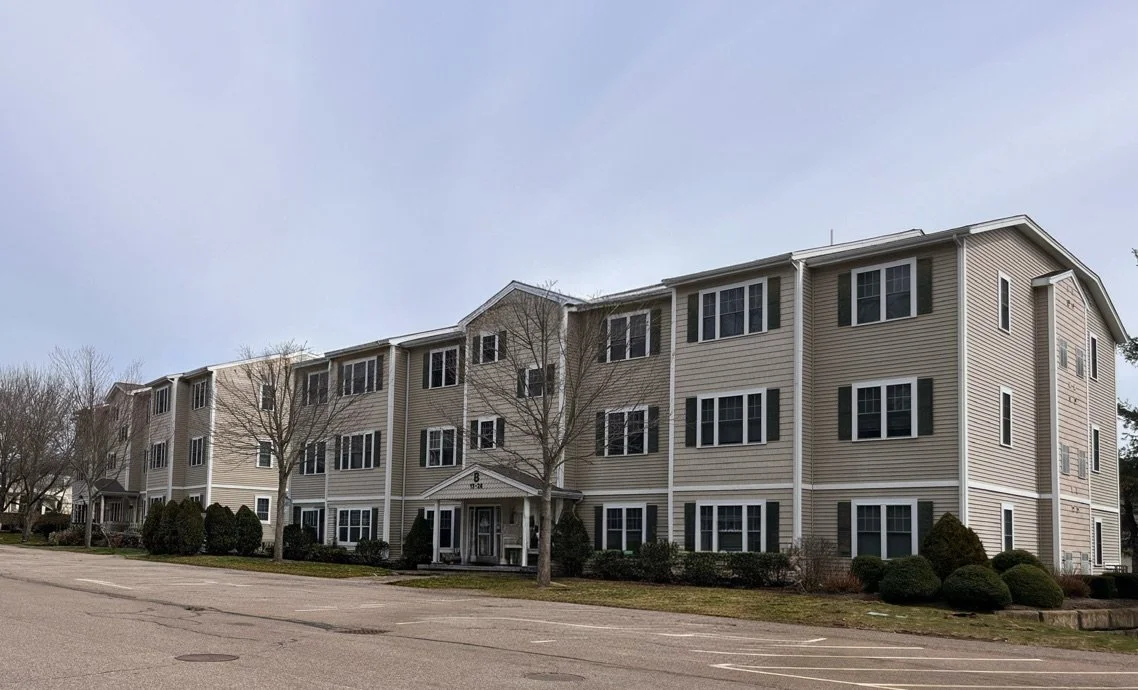A three-story residential apartment building with beige siding and white trim