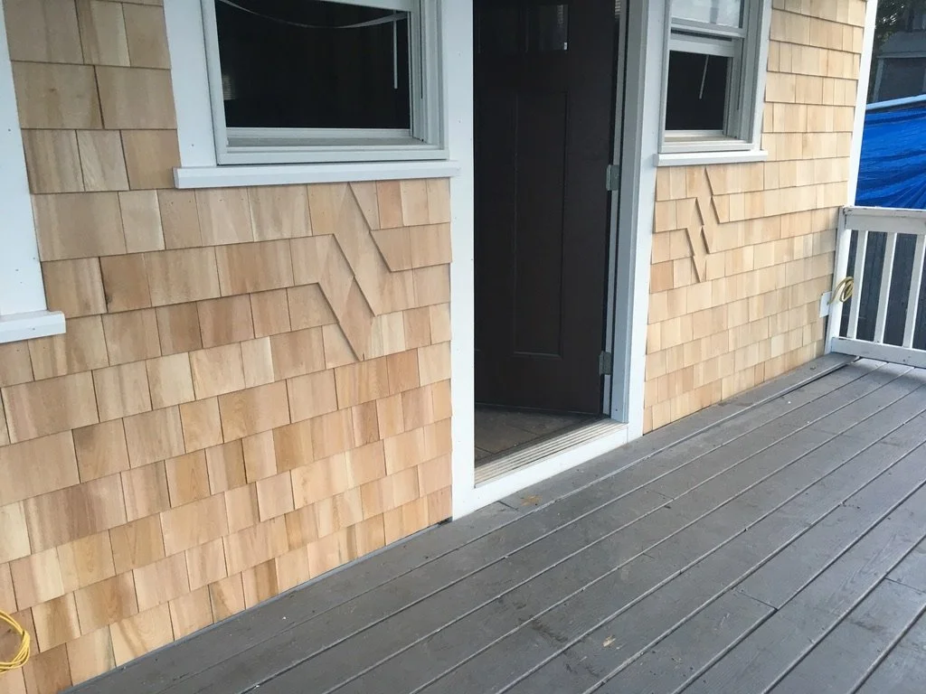 View of a house exterior with wooden siding, a door with a small doormat, and a deck with wooden planks leading to the door.