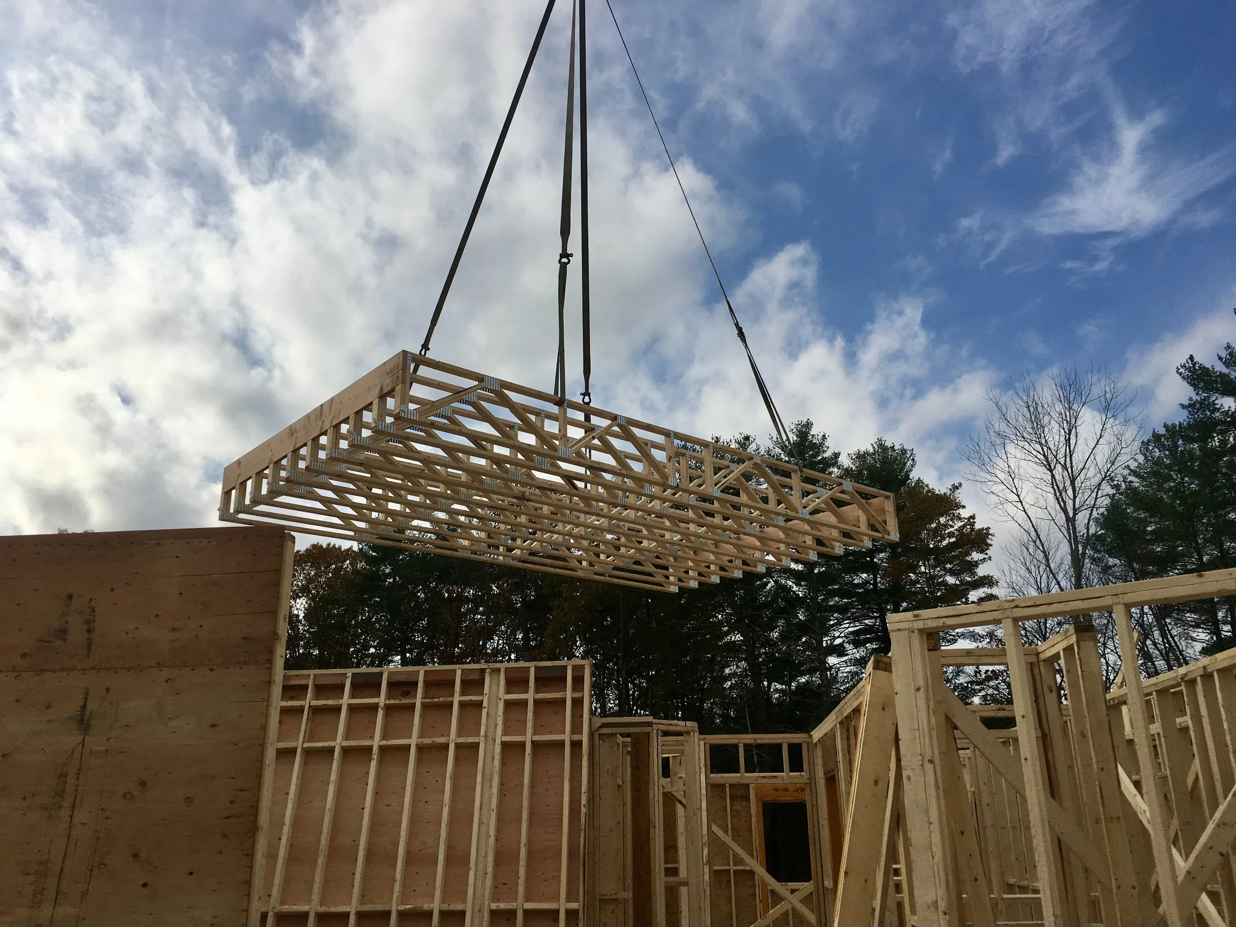 Wooden framing structures under construction with a crane lifting a large wooden truss in a 