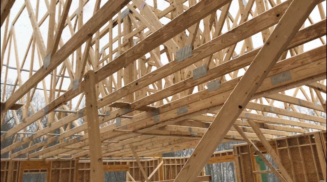 Wooden framing of a building under construction, showing the roof trusses and support beams.