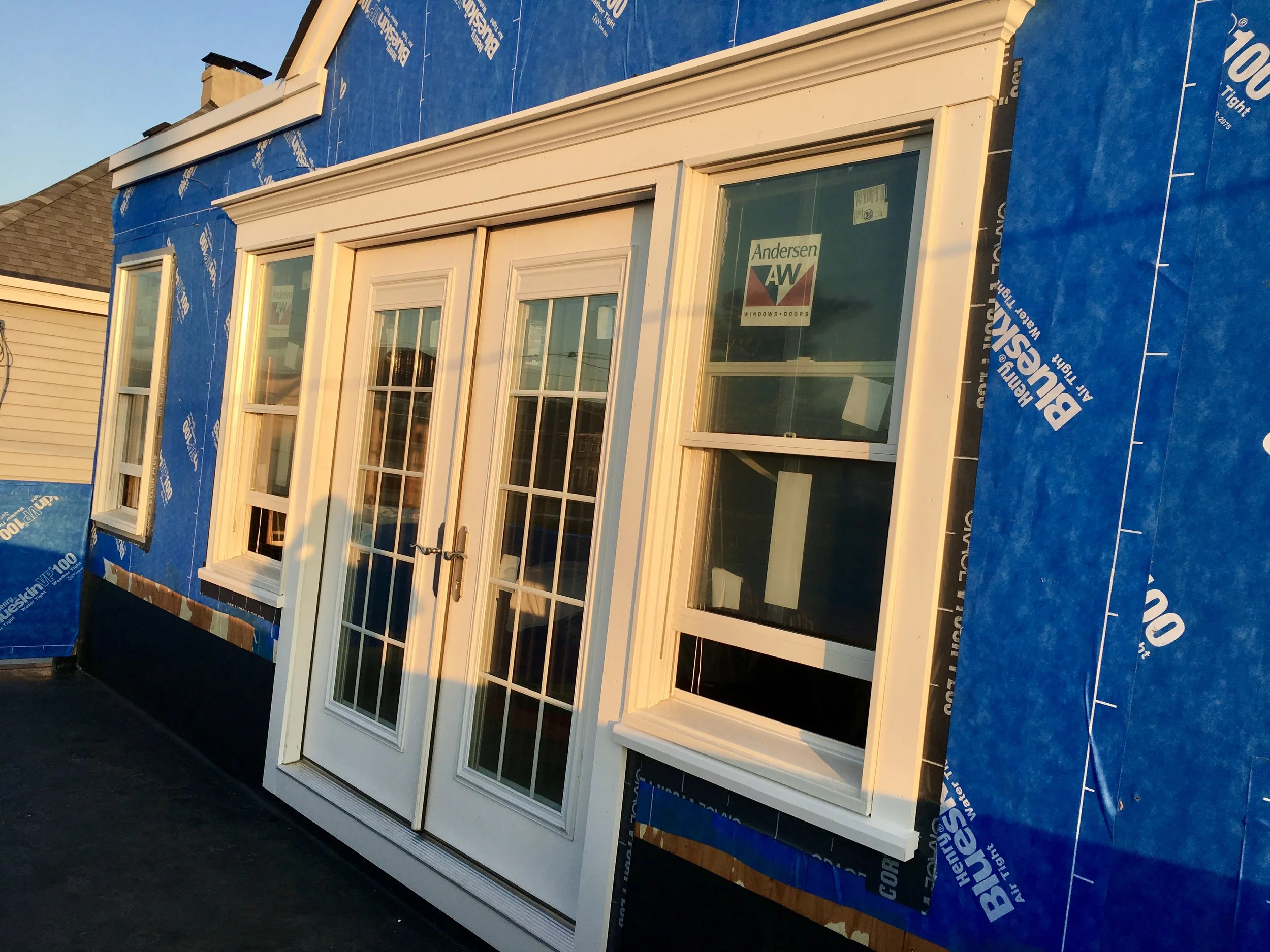 Newly installed white French door with glass panes on a house under construction, surrounded by blue house wrap material.