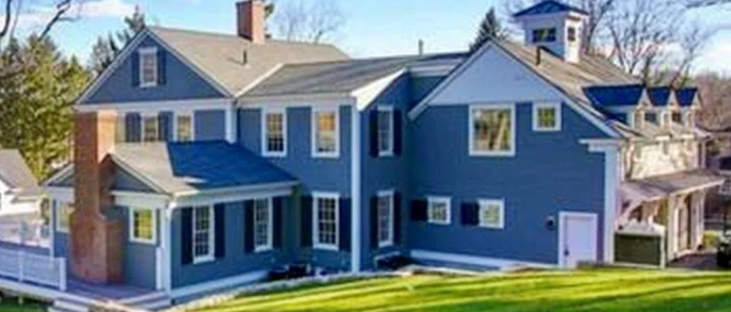 A large blue house with white trim, multiple windows, and a brick chimney