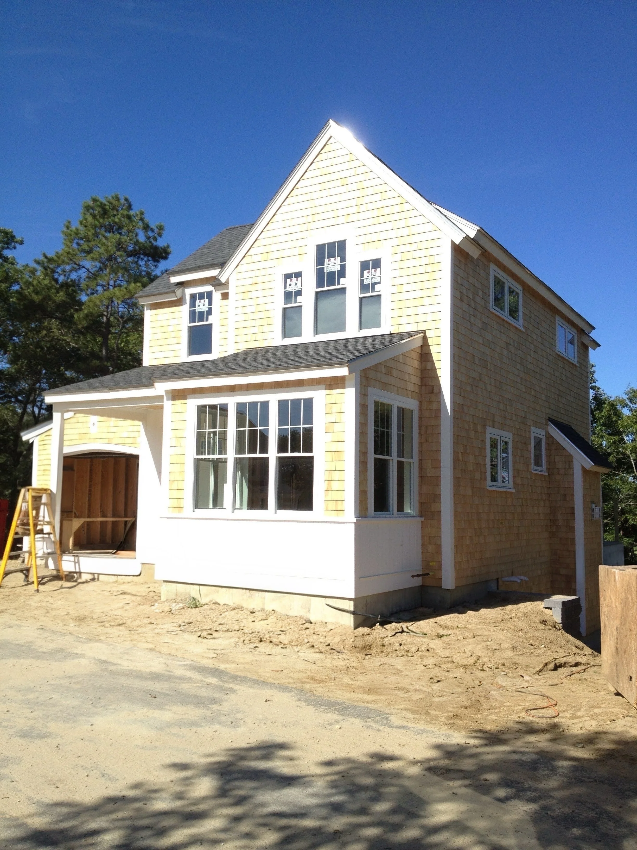 Under construction two-story house with yellow siding, multiple windows, and a covered front porch