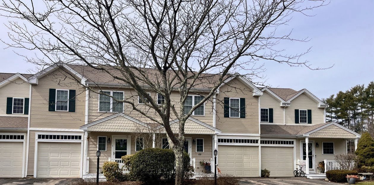 A row of townhouses with beige siding, black shutters, and white accents