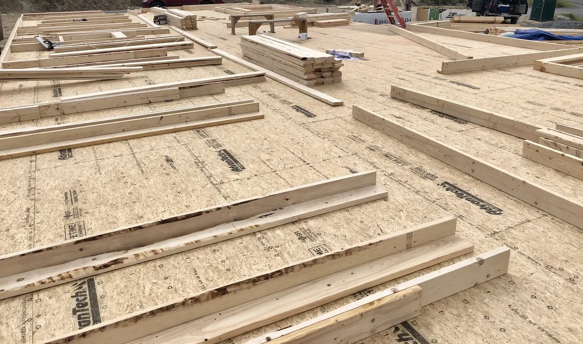 Construction site with wooden framing pieces and plywood on the floor, preparing for building a structure.