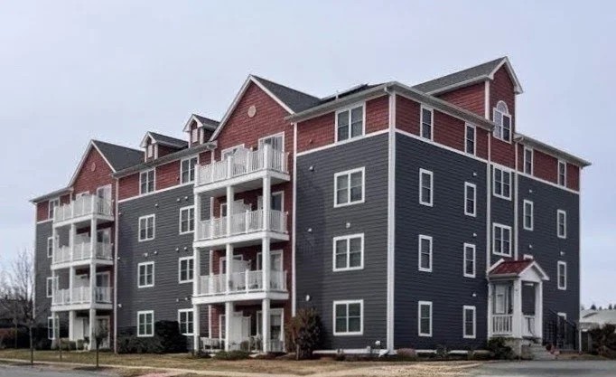 Multi-story apartment building with red and dark gray exterior, white balconies, and multiple windows.
