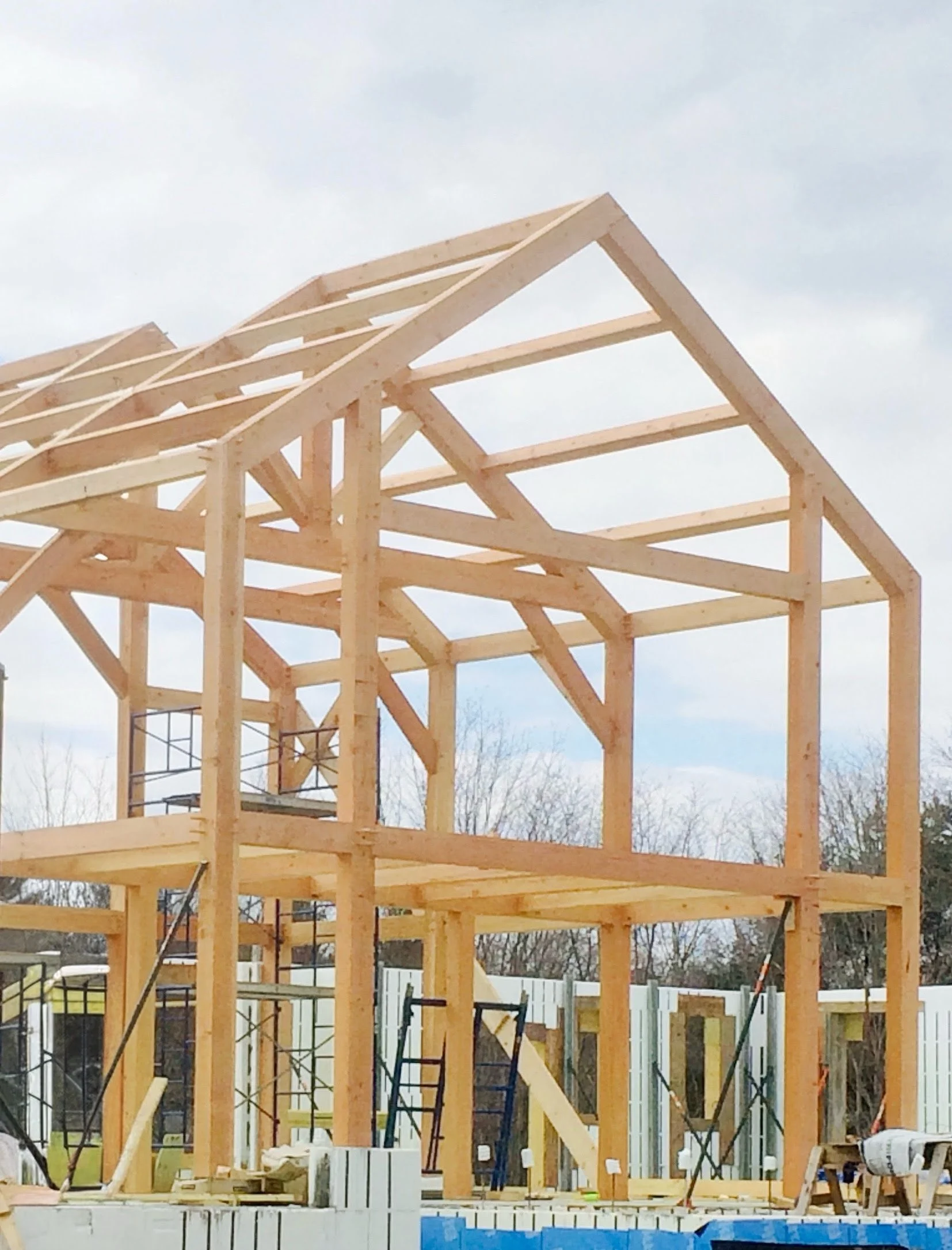 Wooden house framework under construction with exposed beams and roof trusses, at a construction site.