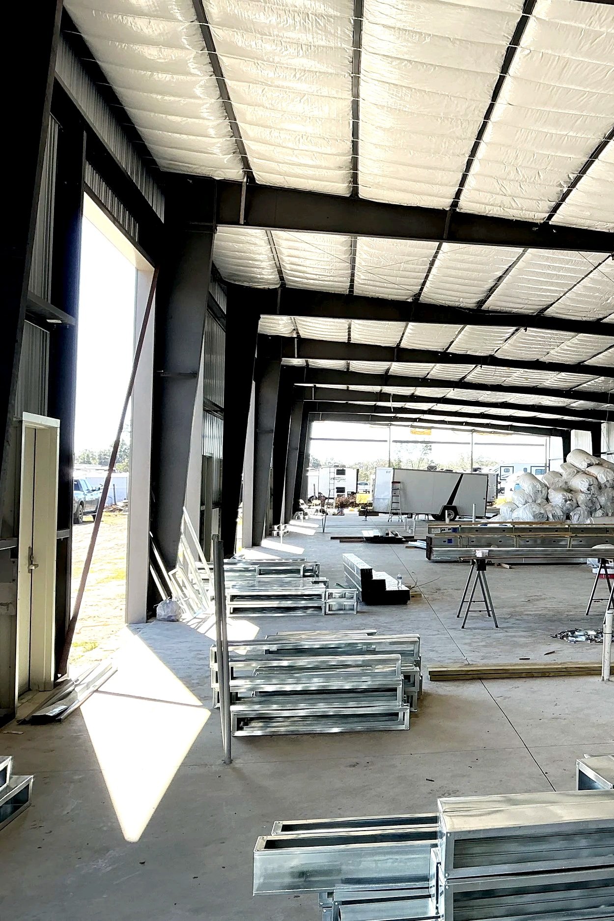 Construction site inside a building with exposed ceiling insulation, metal framing, construction materials, and equipment scattered around.