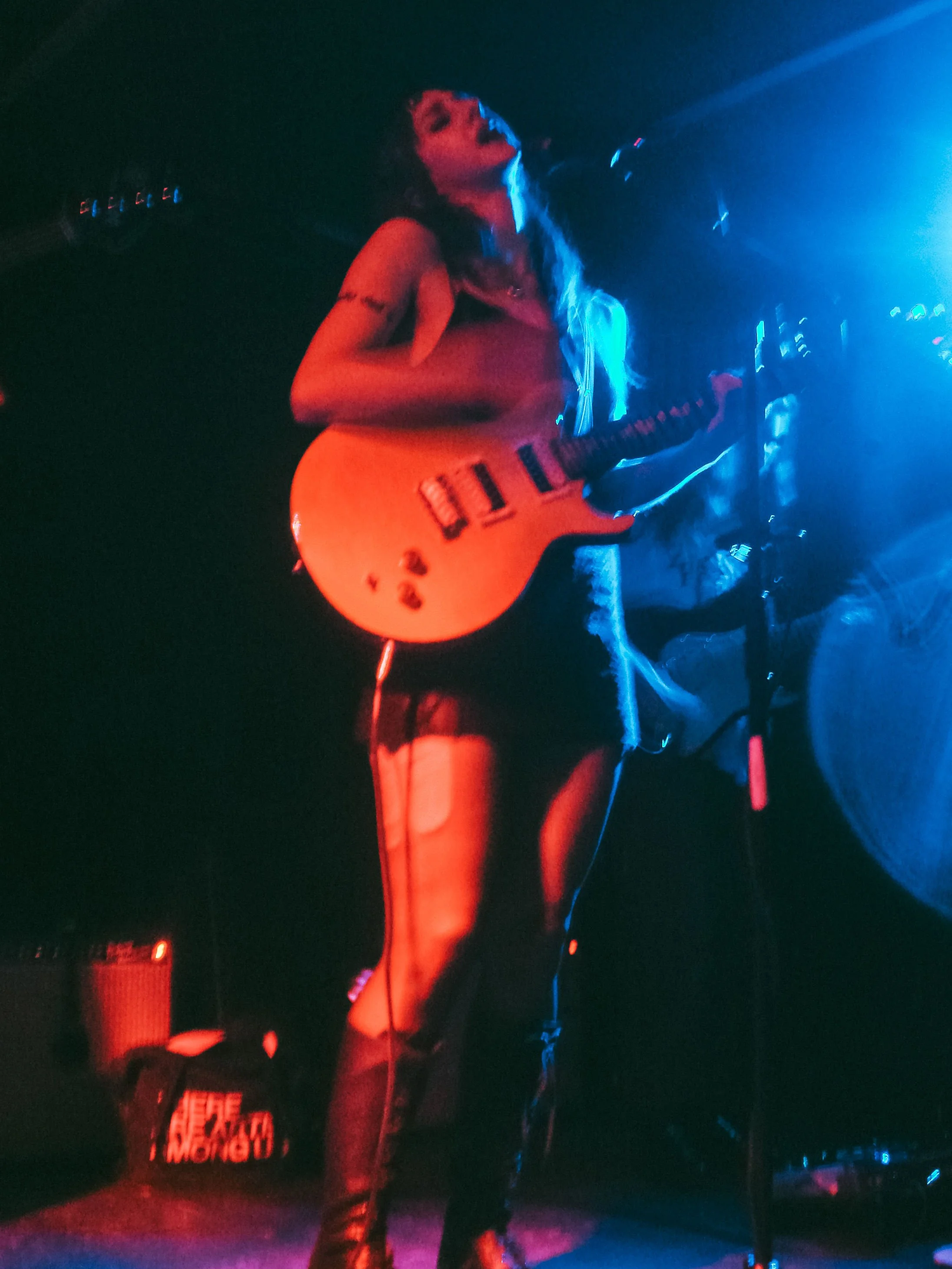 Stupid Lucky Live at Cassette in Ridgewood Queens, NYC - Photo by Beth Crane on Digital Camera. Taylor Pearlstein plays the guitar, lit in blue and red.