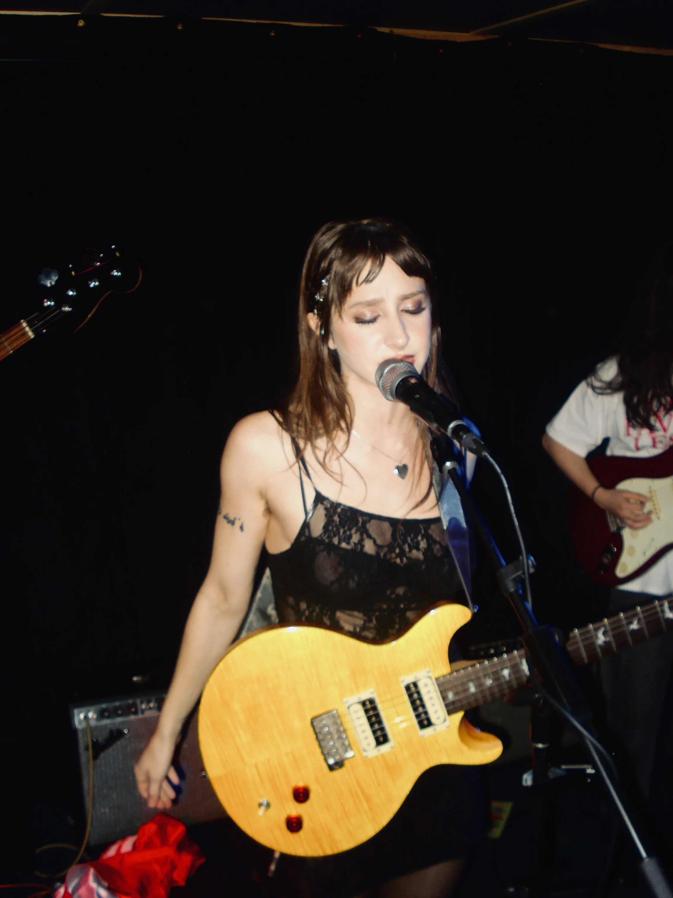 Stupid Lucky Live at Cassette in Ridgewood Queens, NYC - Photo by Beth Crane on Digital Camera. Taylor Pearlstein sings at the mic, her yellow PRS guitar in front of her.