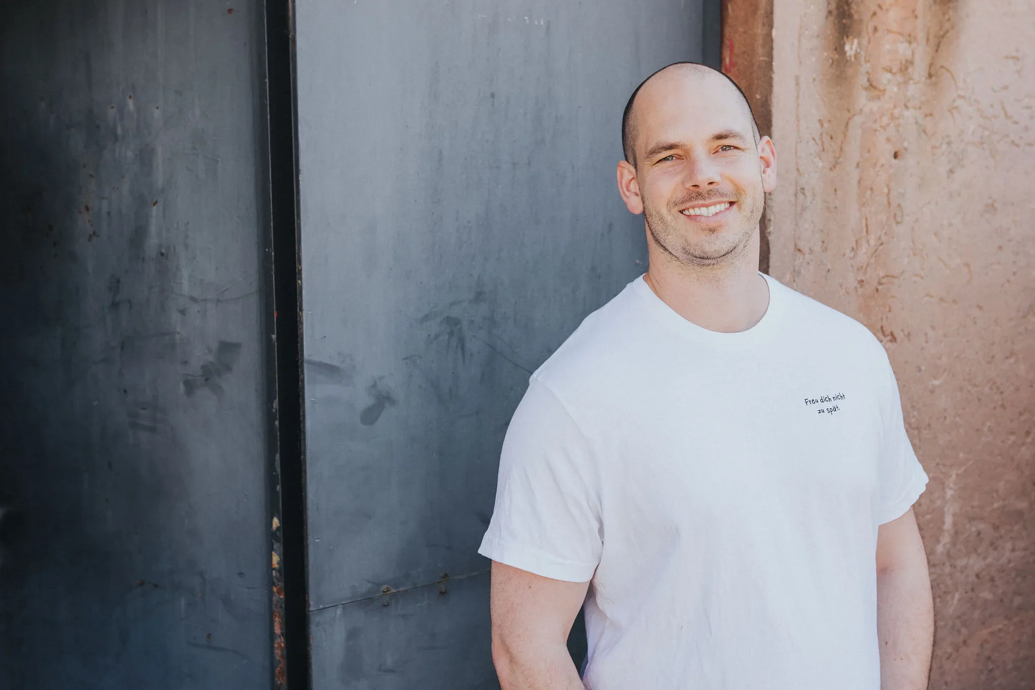 Tim Schröder, coach for inner clarity, standing outdoors against a dark wall and a beige brick wall.