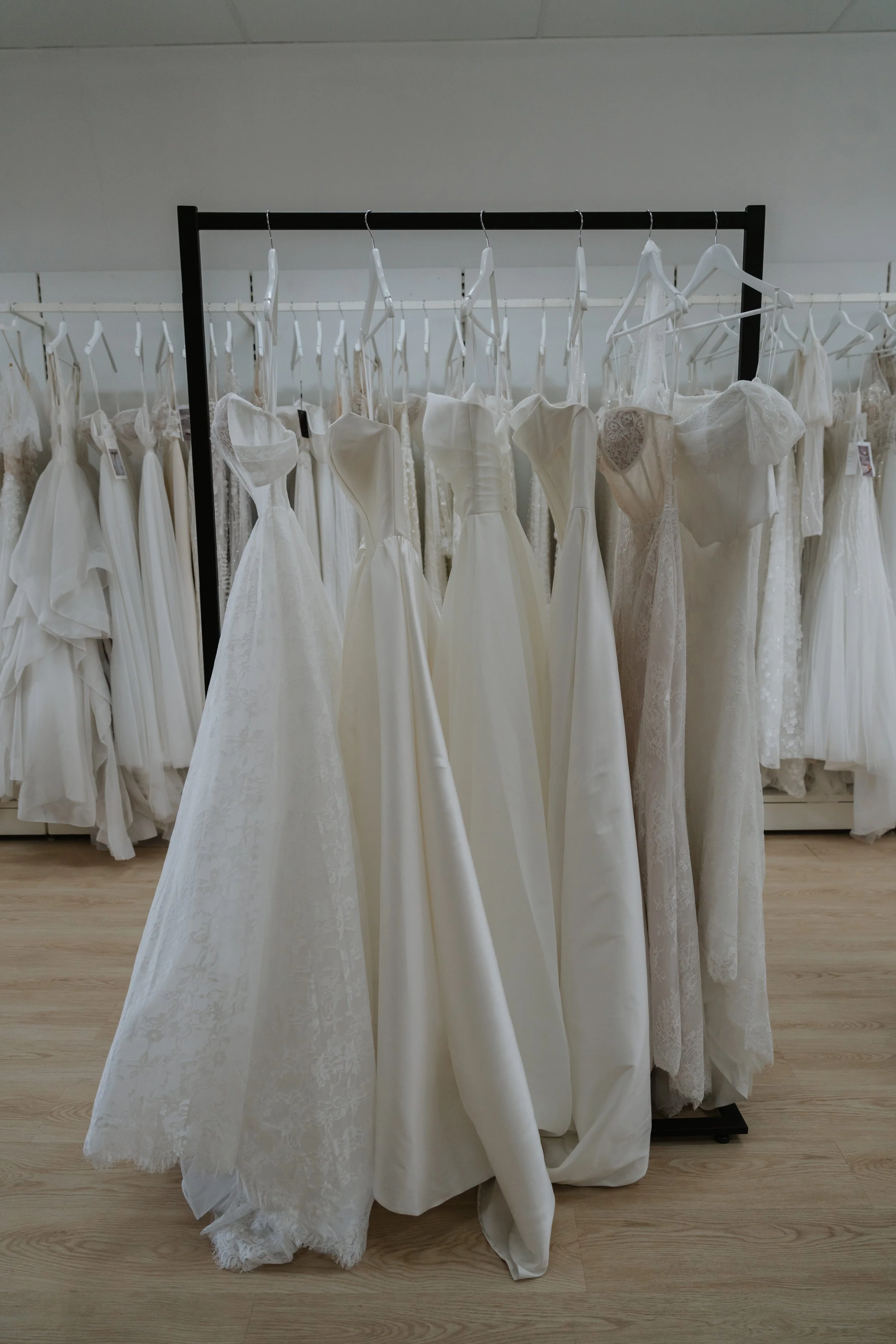A clothing rack displaying multiple white wedding dresses with lace, satin, and tulle fabrics.