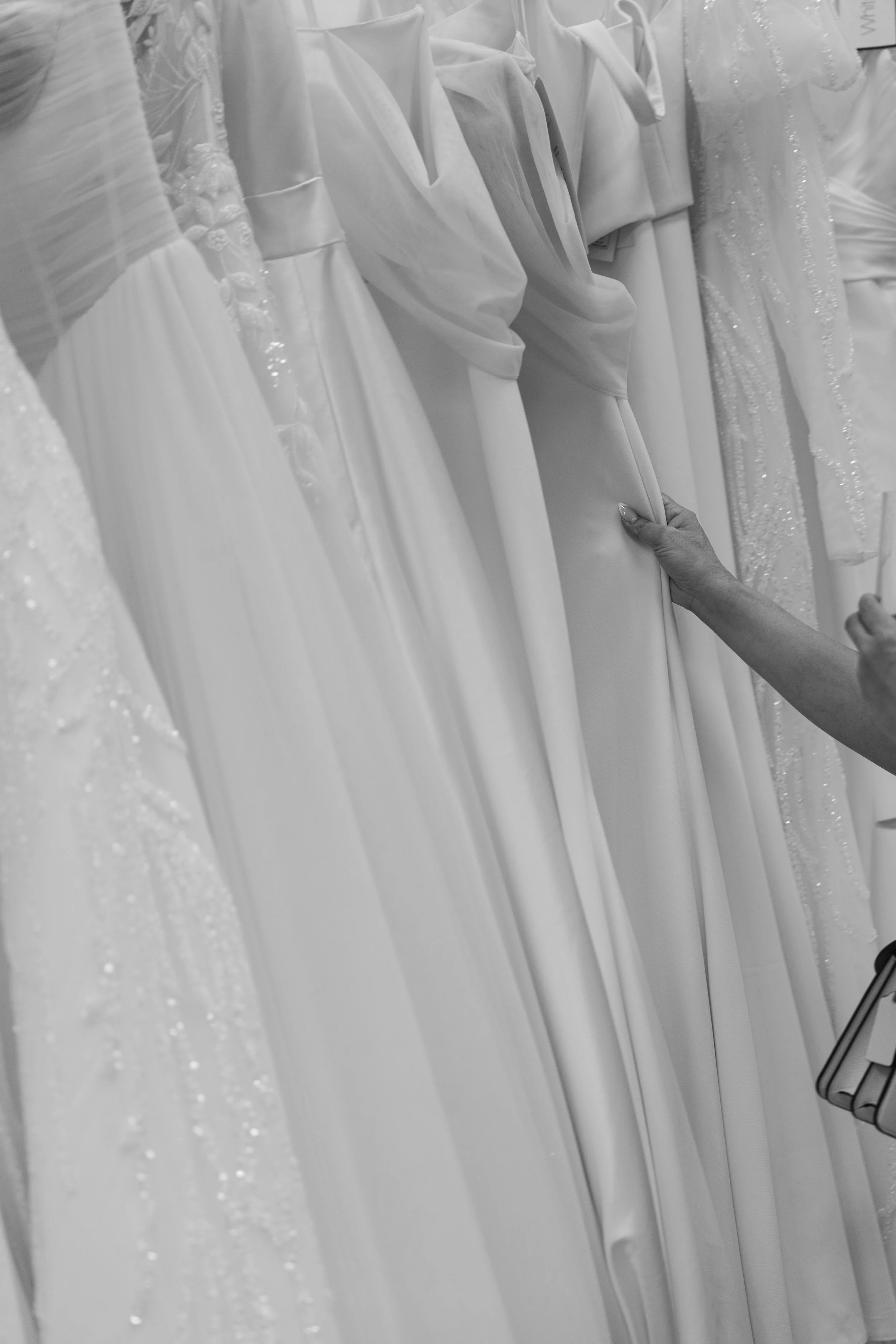 A person shopping for wedding dresses in a bridal boutique, with the dresses hanging on a rack.