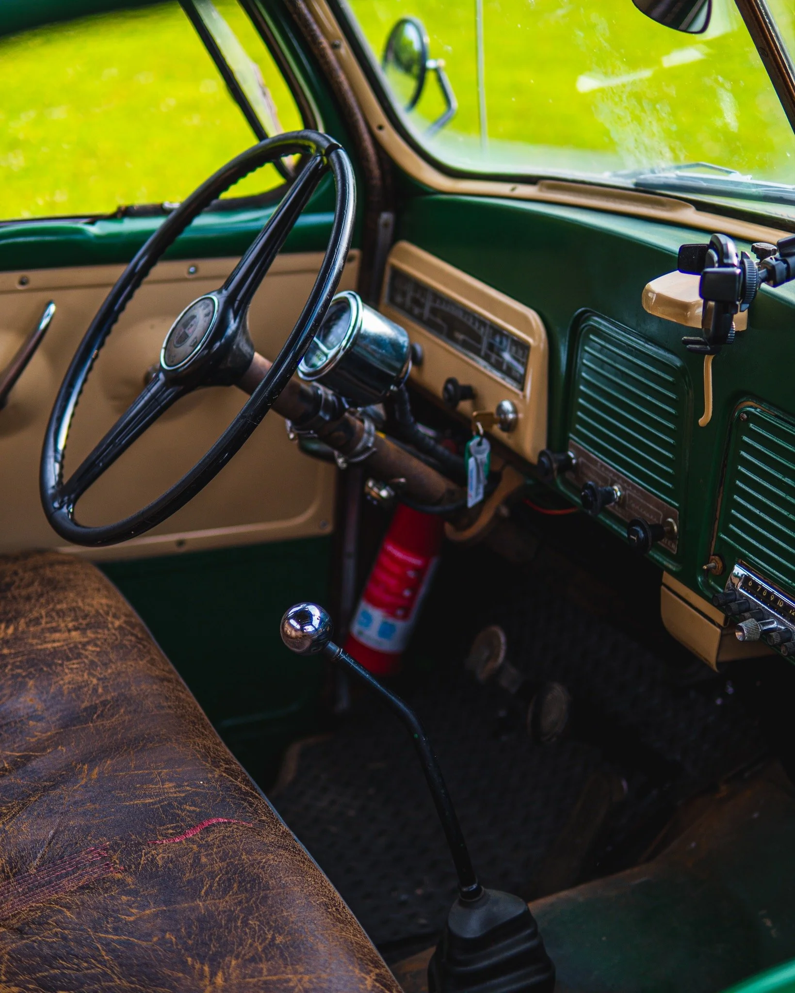 Interior of an old green and beige vintage truck with worn leather seat, steering wheel, dashboard, and gear shift.