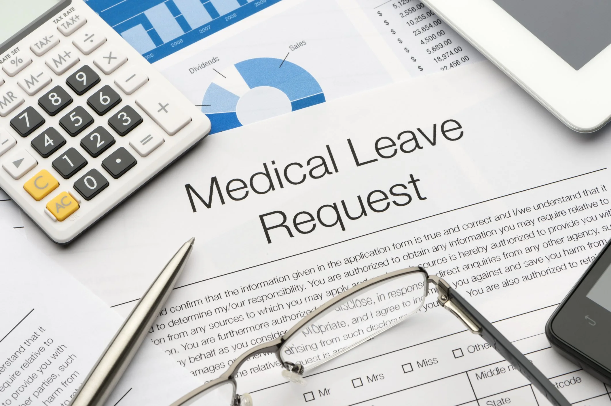 Medical leave request form surrounded by a calculator, pens, eyeglasses, a tablet, and a smartphone on a desk.