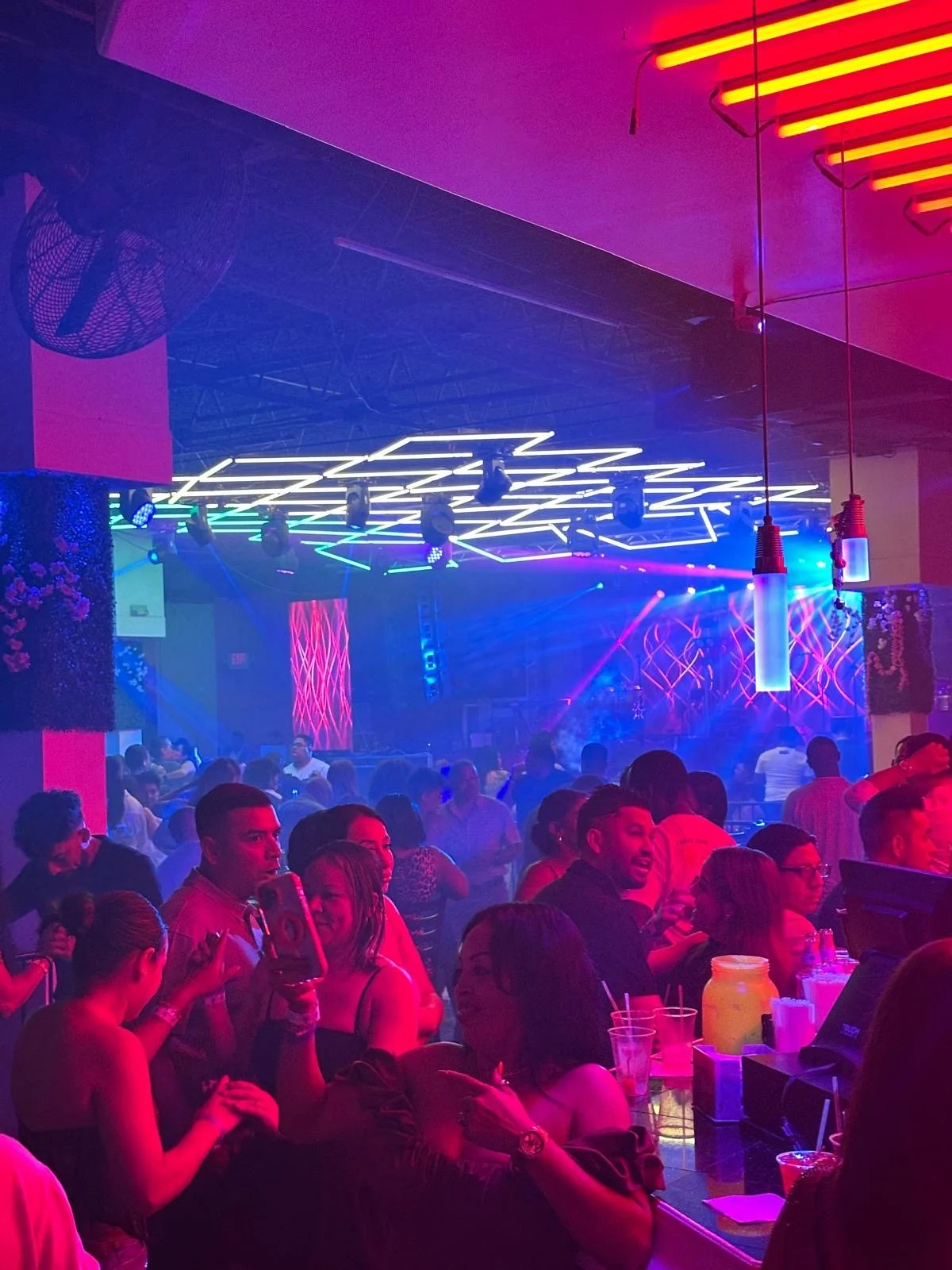 A crowded nightclub with colorful neon lights, a dance floor, and people socializing and enjoying drinks.