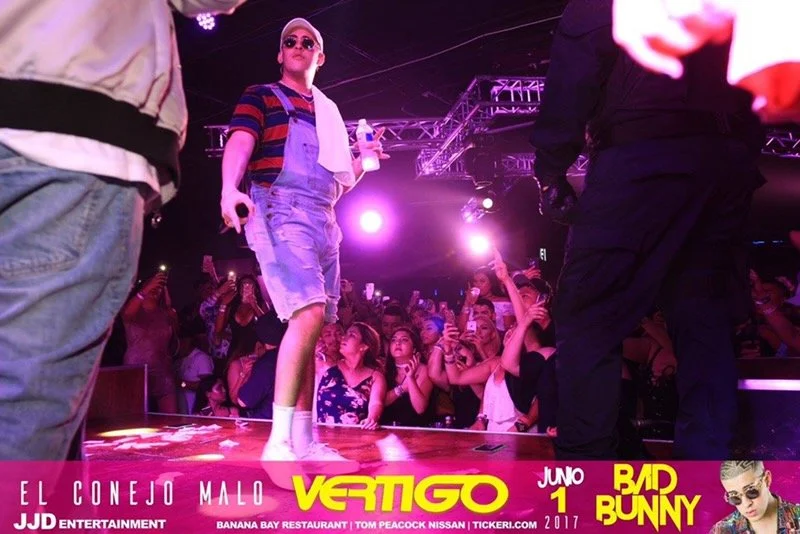 Pop star Bad Bunny performing on stage at a concert with a crowd of fans taking photos with their phones.